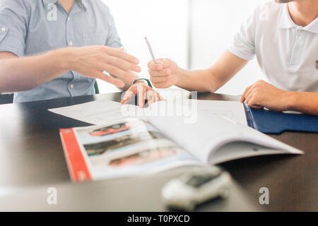 Picture of two men sit at table together. They hold hands on documents. Guy on right gives pen to man on left. There is journal on table. Small white  Stock Photo