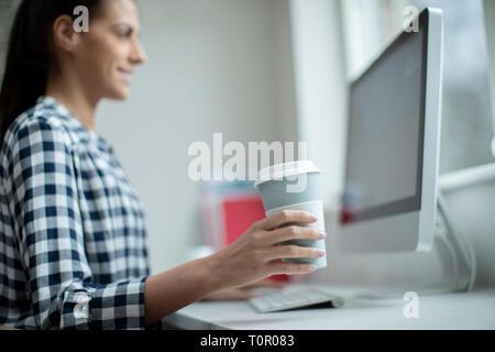 Woman Working At Computer Drinking From Reusable Takeaway Cup Stock Photo