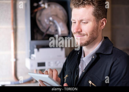 Male Heating Engineer Servicing Central Heating Boiler Using Digital Tablet Stock Photo