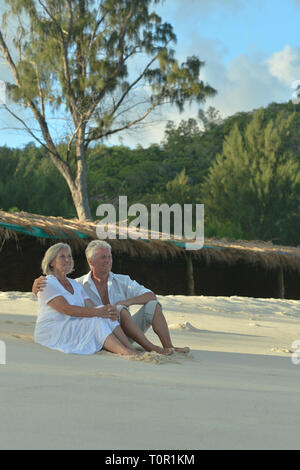 Portrait of happy elderly couple sitting on tropical beach Stock Photo