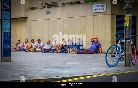 London, UK, Aug 2018, builders sitting down on the pavement at lunchtime, England Stock Photo