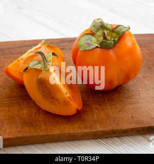 Tasty persimmon on a chopping board on white wooden surface, side view. Close up. Stock Photo