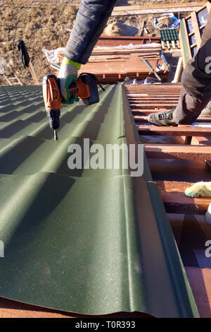 The professional worker works on installation of a roof of a roof by sheets of a metal tile and drills a screw with a drill 2019 Stock Photo