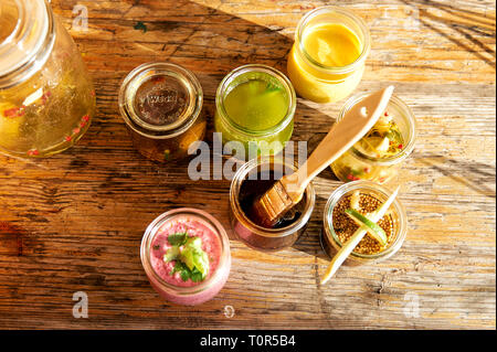 6 Glaesschen mit unterschiedlichen Marinaden und Grillsauchen stehen auf einem Holztisch. Sie wurden frisch zubereitet fuer das Grillvergnuegen Stock Photo