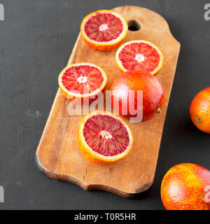 Whole and halved blood oranges on black background, low angle view. Closeup. Stock Photo