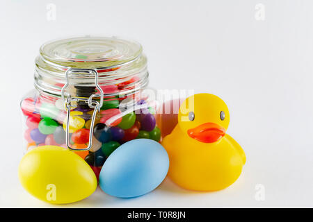 Rubber duck with colorful dyed easter eggs and a jar of jelly beans.  White background.  Copy space above. Stock Photo
