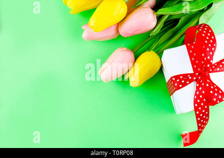 white gift box with red ribbon and tulips on green paper background, top view, copy space, Mother's or father's day card, holiday or birthday concept Stock Photo