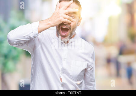 Middle age hoary senior man over isolated background peeking in shock covering face and eyes with hand, looking through fingers with embarrassed expre Stock Photo