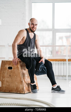 Smiling male athlete sitting at box in gym. Strong fit man resting after intense workout Stock Photo