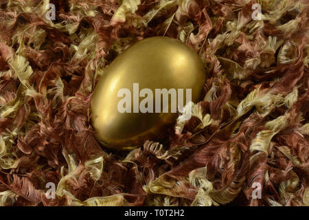 Golden brass Easter egg in nest of brown and golden ribbon yarn Stock Photo