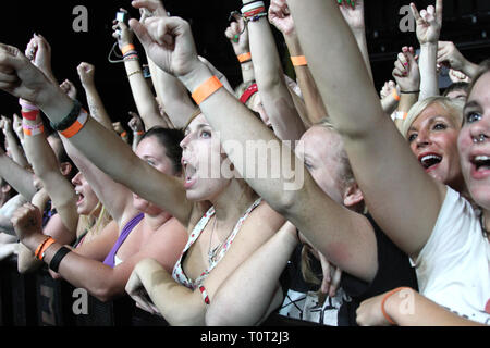 Front row concert fans are shown with their arms raised in the air during the start of a 'live' concert performance. Stock Photo