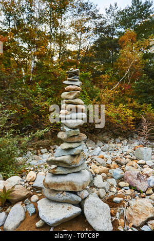 A tall pile of many river stones (cairn) marking a path or trail in the woods. Stock Photo