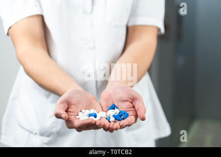 Bright close up of male doctor in uniform with stethoscope and holding blue and white pills in hands Stock Photo