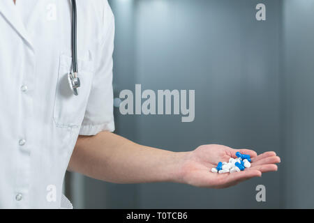 Bright close up of male doctor in uniform with stethoscope and holding blue and white pills in a hand Stock Photo