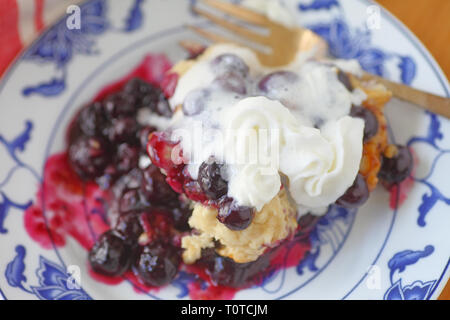 Fresh, warm cobbler with blueberries where whipped cream is melting on contact with hot fruit Stock Photo