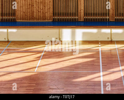 Schooll gym hall with water heating system hidden over wooden bars cover.  Basketball court. Lines of playfield in hall. Stock Photo