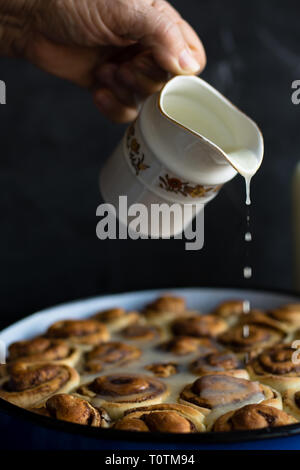 Baker putting sugar glaze syrup on to baked cinnamon buns Stock Photo