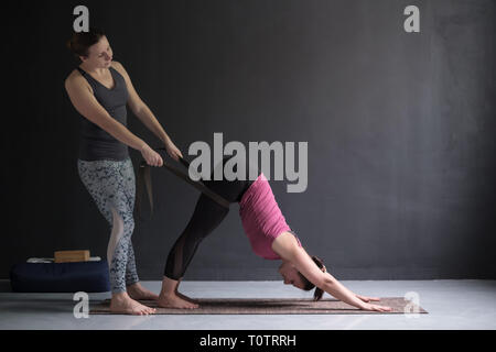 Yoga teacher or pilates instructor helping young woman to stretch muscles. Stock Photo