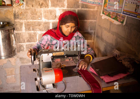 A woman making clothes using an old-fashioned sewing machine. Kakani village, Jodhpur, Rajasthan, India. Stock Photo