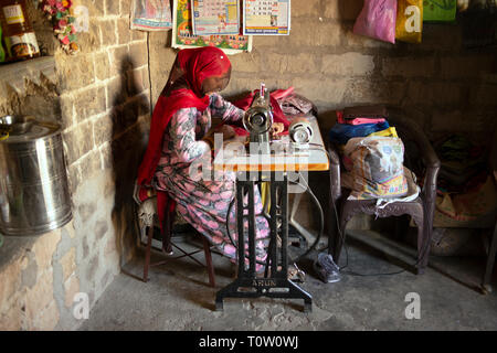 A woman making clothes using an old-fashioned sewing machine. Kakani village, Jodhpur, Rajasthan, India. Stock Photo
