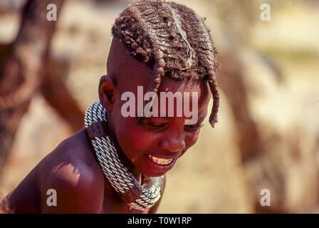 A himba child sports a nice hairstyle with braids and a large metal collar at the Epupa falls in Namibia Stock Photo