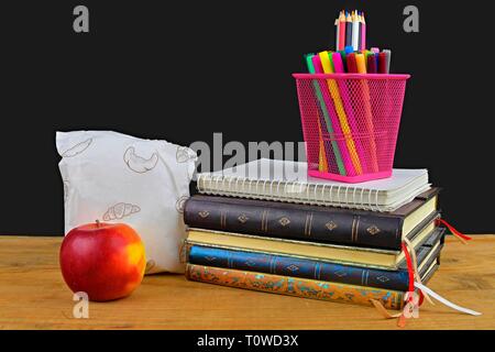 Concept of school lunch break with apple and school supplies on wooden desk, selective focus. Books, markers and color pencils emphasizing the concept Stock Photo