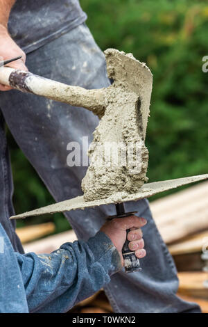 Construction Worker Placing Wet Cement On Platter For Tile Worker At Pool Construction Site. Stock Photo