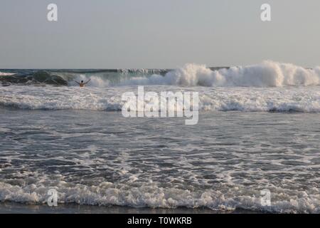 Man standing in ocean holding up his arms with a bit wave about to break on him Stock Photo