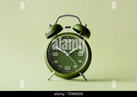 Old fashioned red alarm clock with bells centered over a green background Stock Photo