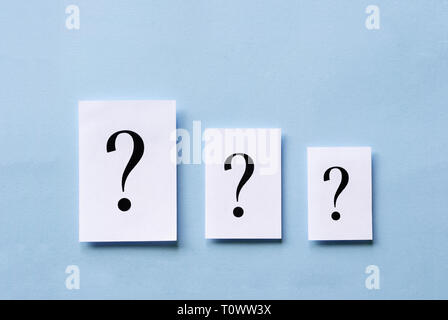 Three white cards with printed question marks arranged in descending size on a blue background in a conceptual image Stock Photo
