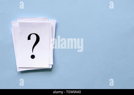 Pile of stacked question marks printed on sheets of white paper or signs arranged to the side on a blue background with copy space in a conceptual ima Stock Photo