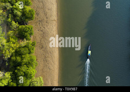 View from above, stunning aerial view of a traditional long tail boat that sails on a river flowing through a green tropical forest. Krabi, Thailand. Stock Photo