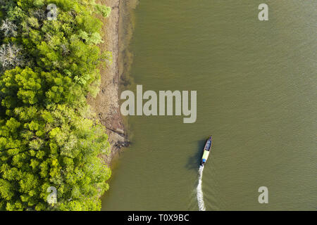 View from above, stunning aerial view of a traditional long tail boat that sails on a river flowing through a green tropical forest. Krabi, Thailand. Stock Photo