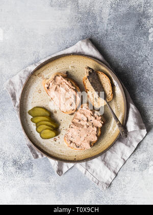 Two toasts duck with prunes rillettes pate on white bread with pickled cucumber slices on vintage plate on gray background. Top view Stock Photo