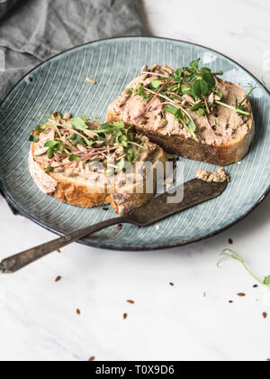 Two toasts duck with prunes rillettes pate on white bread with sprouts and various seeds on a blue plate on white background Stock Photo