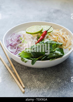 Traditional Vietnamese soup- pho ga in white bowl with chicken and rice noodles, mint and cilantro, green and red onion, chili, bean sprouts and lime 