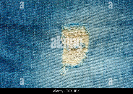 Hole and threads on denim jeans. Ripped  blue jeans background. Close up blue jeans texture. Stock Photo