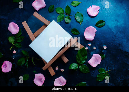Artist easel with rose petals and leaves on a wet background with copy space. Blank template for a watercolor painting Stock Photo