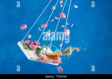 Rose tea with macaron cookies and pink flower petals on swings in motion. Action high speed photogrpahy with hot drinks Stock Photo