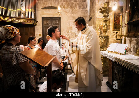 Priest of the Church of Holy Sepulchre gives holy communion to faithful man with other believers waiting for their turn. Christians serving communion. Stock Photo