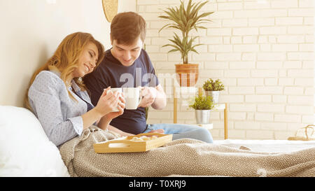 Young couple has breakfast in bed drinks tasty coffee miling in bedroom Stock Photo