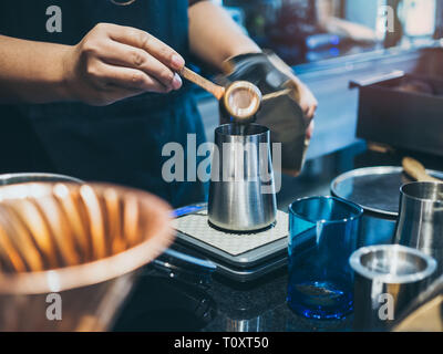 Barista's hand putting ground coffee in stainless steel manual coffee grinder in coffee shop. Stock Photo