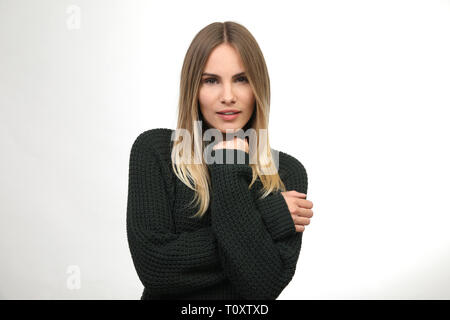 Beautiful blond woman in dark green knit sweater raises her hand