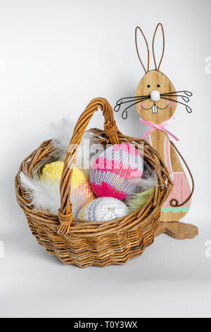 Colorful wooden easter bunny with a wicker basket filled with knitted easter eggs. Stock Photo