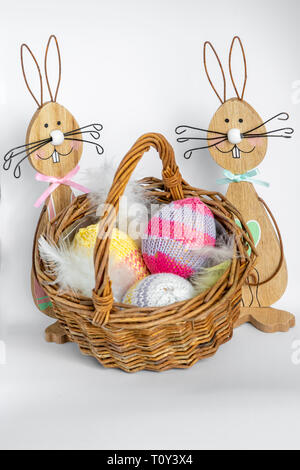 Two colorful wooden easter bunnies with a wicker basket filled with knitted easter eggs. Stock Photo