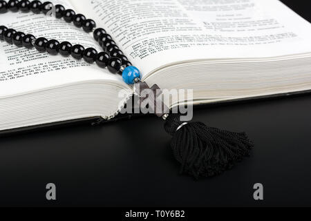 Closeup of opened Holy Bible and rosary beads with cross on black background. Religion concept. Cyrillic text. Stock Photo
