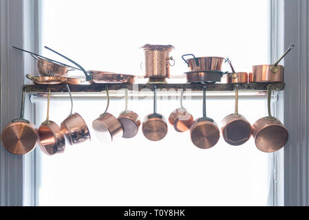 a collection of copper post and pans hangs down in a kitchen. Stock Photo