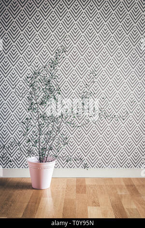 Corokia plant in a pink ceramic pot, near a wall with stylish wallpaper. Scandinavian design. Stock Photo