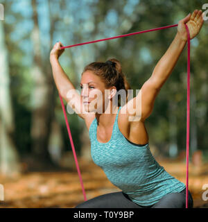 Woman exercising squats with elastic band outdoors, in public park. Stock Photo