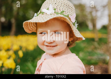 cute blonde little girl smiling with yellow daffodils in the spring country. Stock Photo